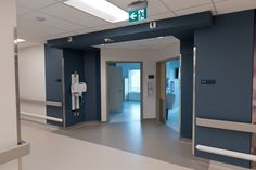 an empty hospital hallway with blue walls and white doors on either side of the room