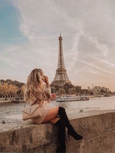 a woman sitting on the edge of a wall looking at the eiffel tower