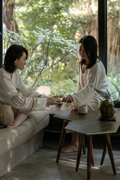 two women in robes sitting on couches and one is holding a cup with tea