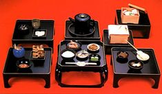 four black trays with food on them sitting on top of a red tablecloth