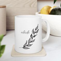 a white coffee mug sitting on top of a counter next to a bowl of fruit