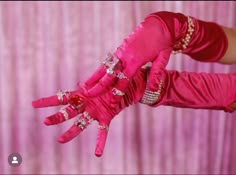 a woman wearing pink gloves and holding up her hands with jewels on the fingers in front of a curtain