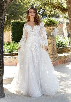 a woman in a wedding dress standing next to a tree with her hands on her hips