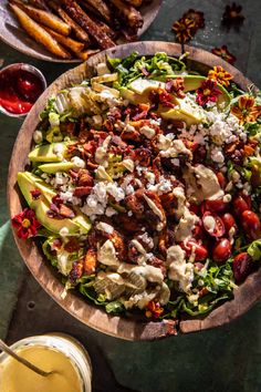 a large salad with dressing in a wooden bowl on a table next to other food