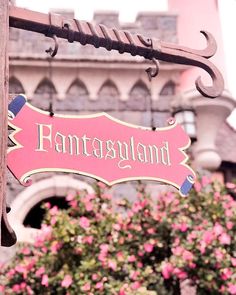 a pink sign hanging from the side of a wooden pole with flowers in front of it