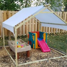 a child's play area in the backyard with a white tent and slide set