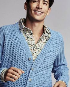 a man in a blue cardigan is smiling and holding his hand on his hip