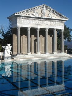 an old building with columns and statues on the side of it, reflected in a pool