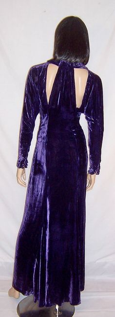 This is a stunning, violet silk velvet gown with a modified halter neckline and triangular cut-outs in both the front and the back of the bodice. The bodice is fitted and adorned with clear rhinestones. The gown is cut on the bias and has a series of snaps for closure on the left side. There are also two snaps at the back of the neckline for closure. The gown is dramatic and flattering and would be comparable to a modern day Size 6. It is in excellent vintage condition. Velvet Fitted Wedding Gown, Glamorous Velvet Gown For Wedding, Fitted Velvet Wedding Gown, Purple Velvet Party Dress, Purple Velvet Dress For Party, Fitted Glamorous Velvet Gown, Purple Fitted Evening Gown, Purple Velvet Fitted Dress, Glamorous Fitted Velvet Gown