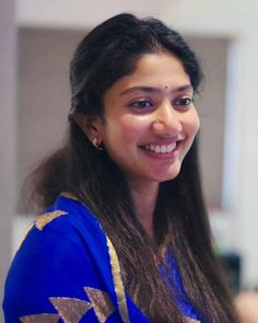 a woman with long dark hair wearing a blue sari and smiling at the camera