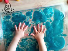 two hands reaching for blue liquid in a plastic tray with gummy bears on it