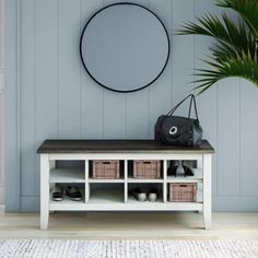 a white bench with baskets underneath it and a round mirror on the wall behind it