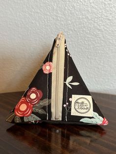 a small triangle shaped bag with floral print on it sitting on a wooden table next to a white wall