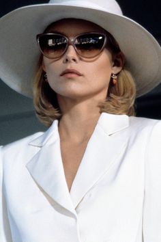 a woman in a white suit and hat with sunglasses on her head looking off to the side