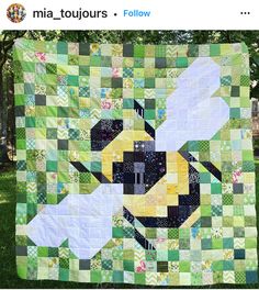 a green and yellow patchwork quilt with a bee in the center on top of it