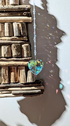 a heart shaped glass ornament hanging from a chain on a piece of wood