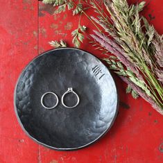 two wedding rings sitting on top of a black plate next to some flowers and grass