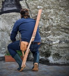 a man is leaning against a rock with a large wooden stick in his right hand