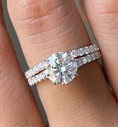 a woman's hand with a diamond ring on top of her finger and the other hand holding an engagement ring