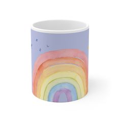 a coffee mug with a rainbow painted on the side and birds flying over it, against a blue sky