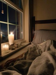 a candle is lit in front of a window with a blanket on the bed next to it