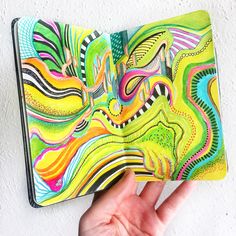 a hand holding an open notebook with colorful swirls on the cover and inside it