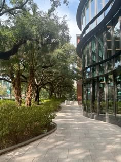 an empty sidewalk in front of a building with glass walls and trees on both sides