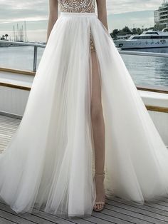 a woman standing on top of a wooden deck wearing a white dress with high slit