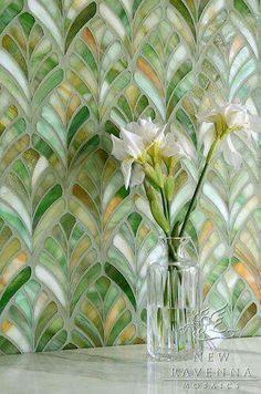 two white flowers in a glass vase against a wall with green and yellow mosaic tiles