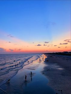 people are walking on the beach at sunset