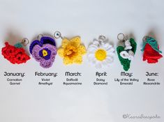 six crocheted flower keychains with names in different colors and sizes, arranged on a white surface