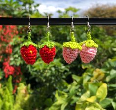 three crocheted strawberries hanging from a clothes line in front of some bushes