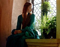 a woman with long red hair sitting on a window sill in a green dress