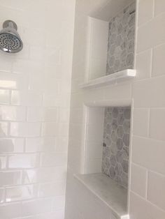 a white tiled bathroom with shelves on the wall and shower head mounted to the side