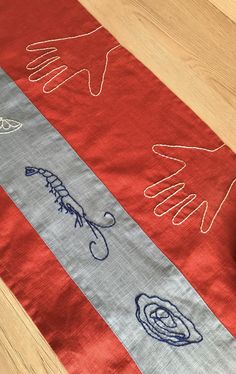 a red table runner with hand drawn designs on it and a bowl of fruit next to it