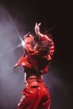 a woman in red is dancing on stage with her arms up to the ceiling and head down