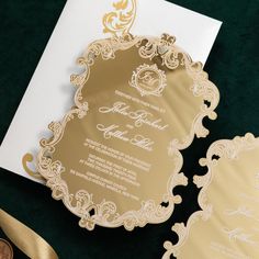 a gold and white wedding card on top of a green table