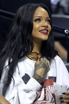 a woman with long black hair and tattoos sitting in the stands at a basketball game