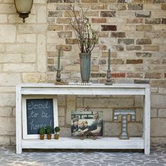 a white shelf with pictures and plants on it in front of a brick wall next to a potted plant