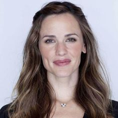 a woman with long brown hair wearing a black shirt and smiling at the camera while standing in front of a white background