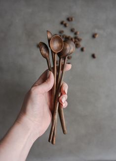 a person holding three wooden spoons with coffee beans scattered around them in the background