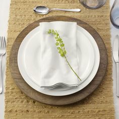 a white plate topped with a green plant on top of a wooden place mat next to silverware