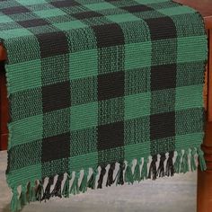 a green and black checkered table cloth with tassels on a wooden chair