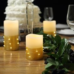 three lit candles sitting on top of a wooden table next to white flowers and greenery