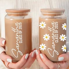 two women holding up jars with flowers on the side and one has a straw in it