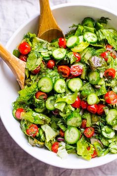 a white bowl filled with cucumber and tomato salad next to a wooden spoon