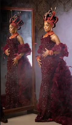 a woman wearing a red dress and headpiece standing in front of a large mirror