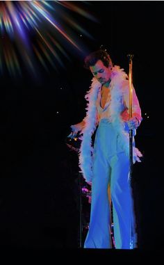 a man in a white feathered suit on stage with a microphone and lights behind him