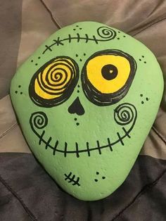 a painted rock with a green face and swirls on it's eyes is sitting on a bed