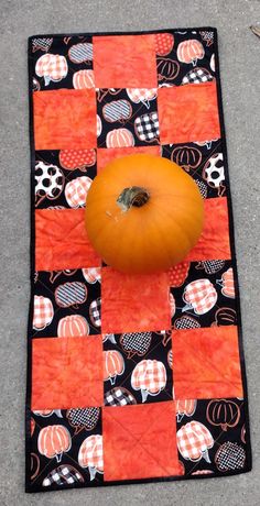 an orange pumpkin sitting on top of a patchwork quilt